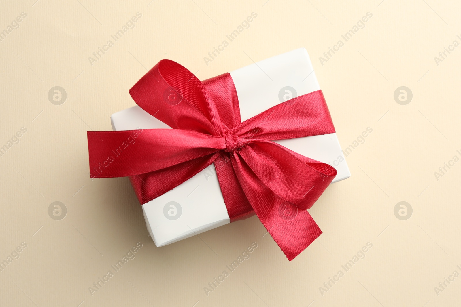 Photo of Beautiful gift box with red bow on beige background, top view