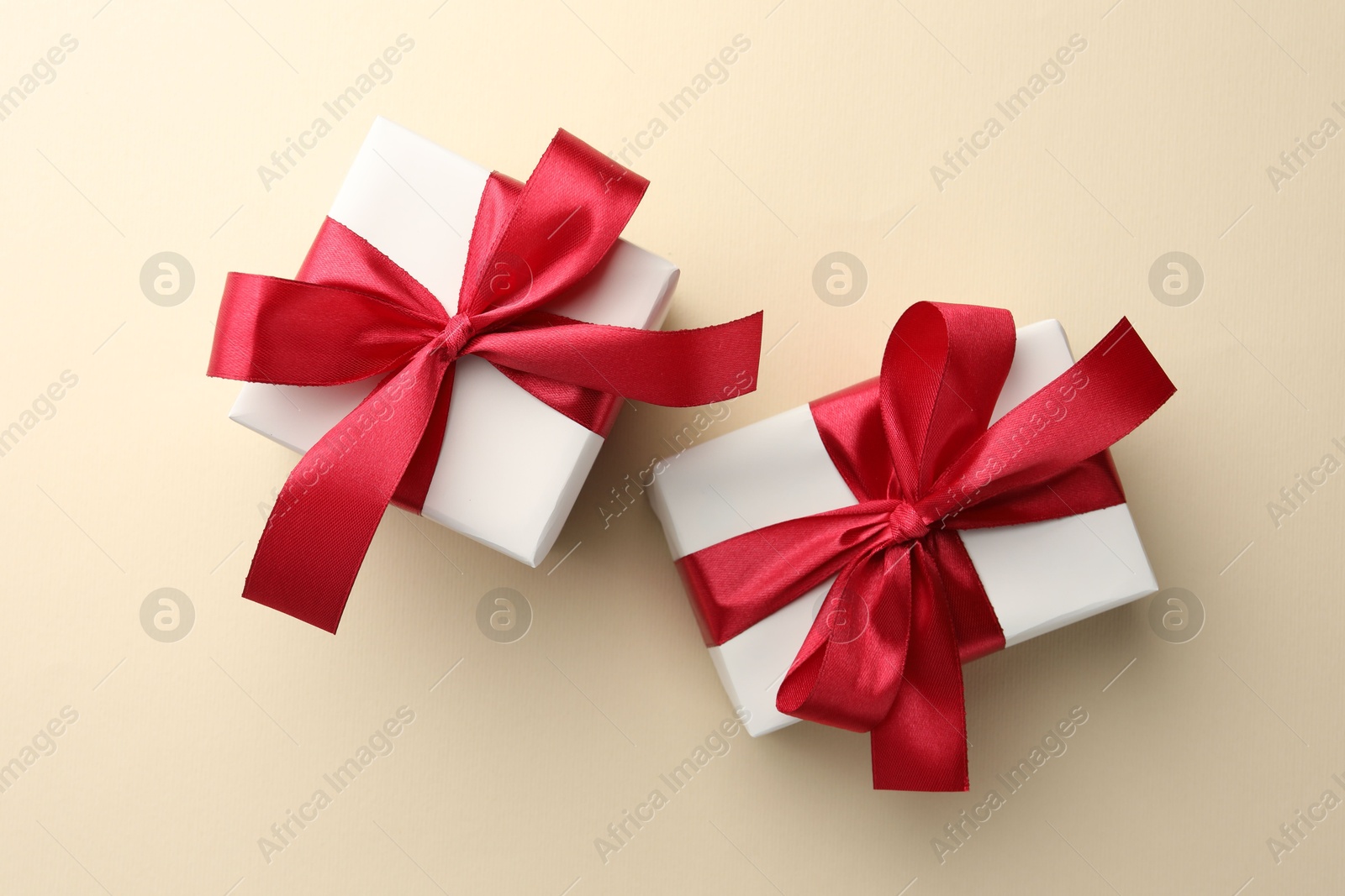 Photo of Beautiful gift boxes with red bows on beige background, top view