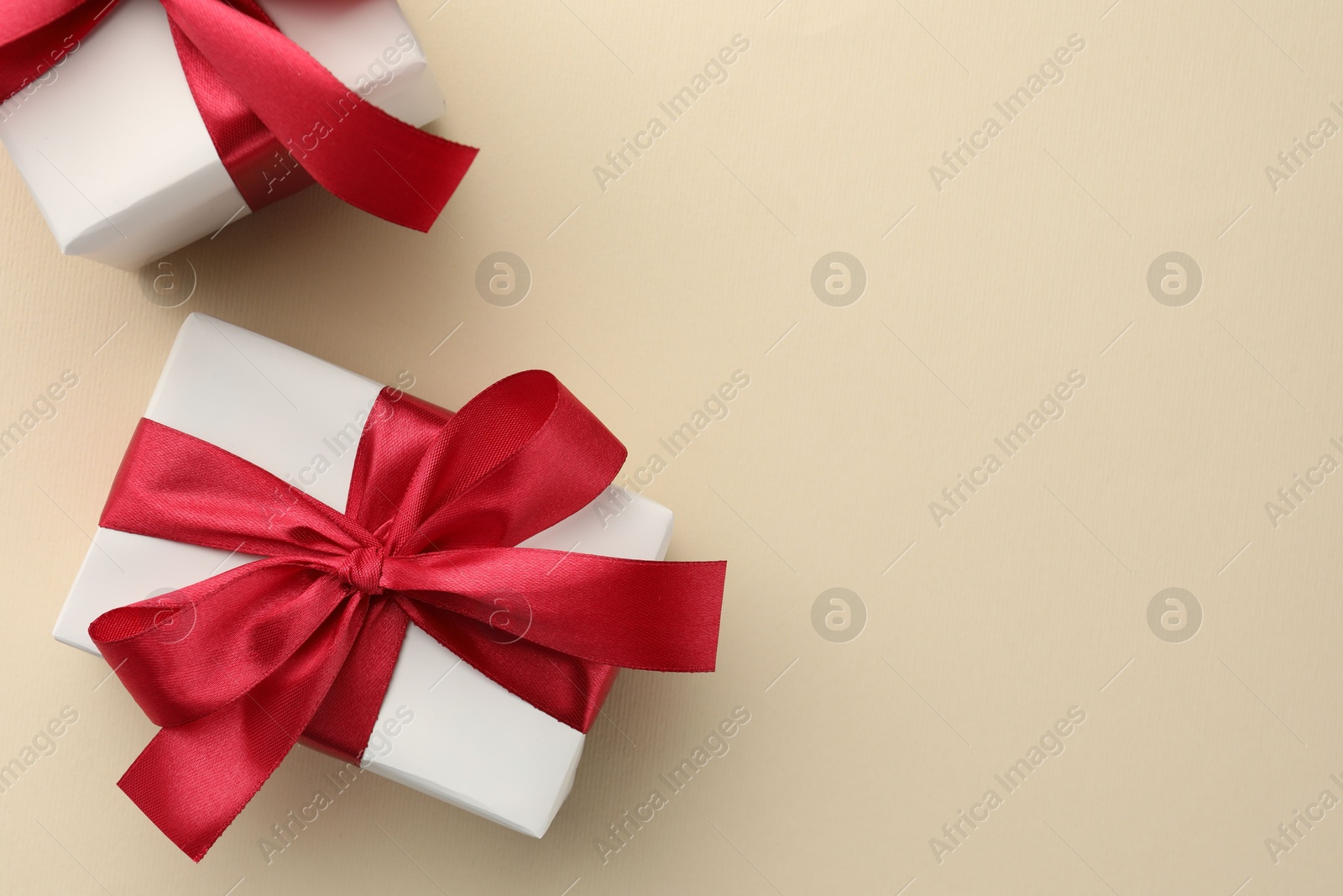 Photo of Beautiful gift boxes with red bows on beige background, top view. Space for text