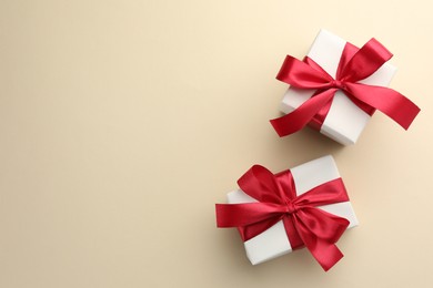 Photo of Beautiful gift boxes with red bows on beige background, top view. Space for text