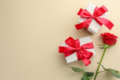 Beautiful gift boxes with red bows and rose on beige background, flat lay. Space for text