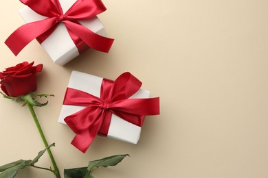 Photo of Beautiful gift boxes with red bows and rose on beige background, flat lay. Space for text