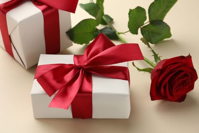 Photo of Beautiful gift boxes with red bows and rose on beige background, closeup