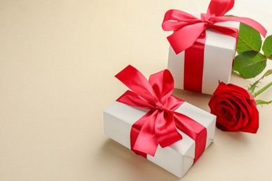 Photo of Beautiful gift boxes with red bows and rose on beige background, space for text