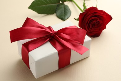 Photo of Beautiful gift box with red bow and rose on beige background, closeup