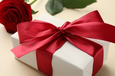 Beautiful gift box with red bow and rose on beige background, closeup