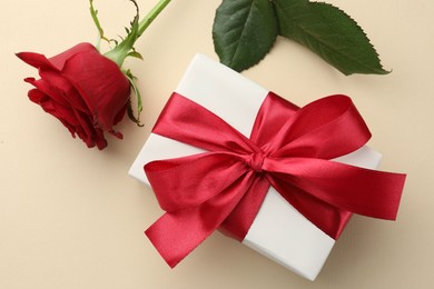 Photo of Beautiful gift box with red bow and rose on beige background, top view