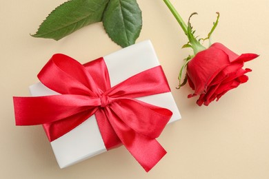 Photo of Beautiful gift box with red bow and rose on beige background, top view