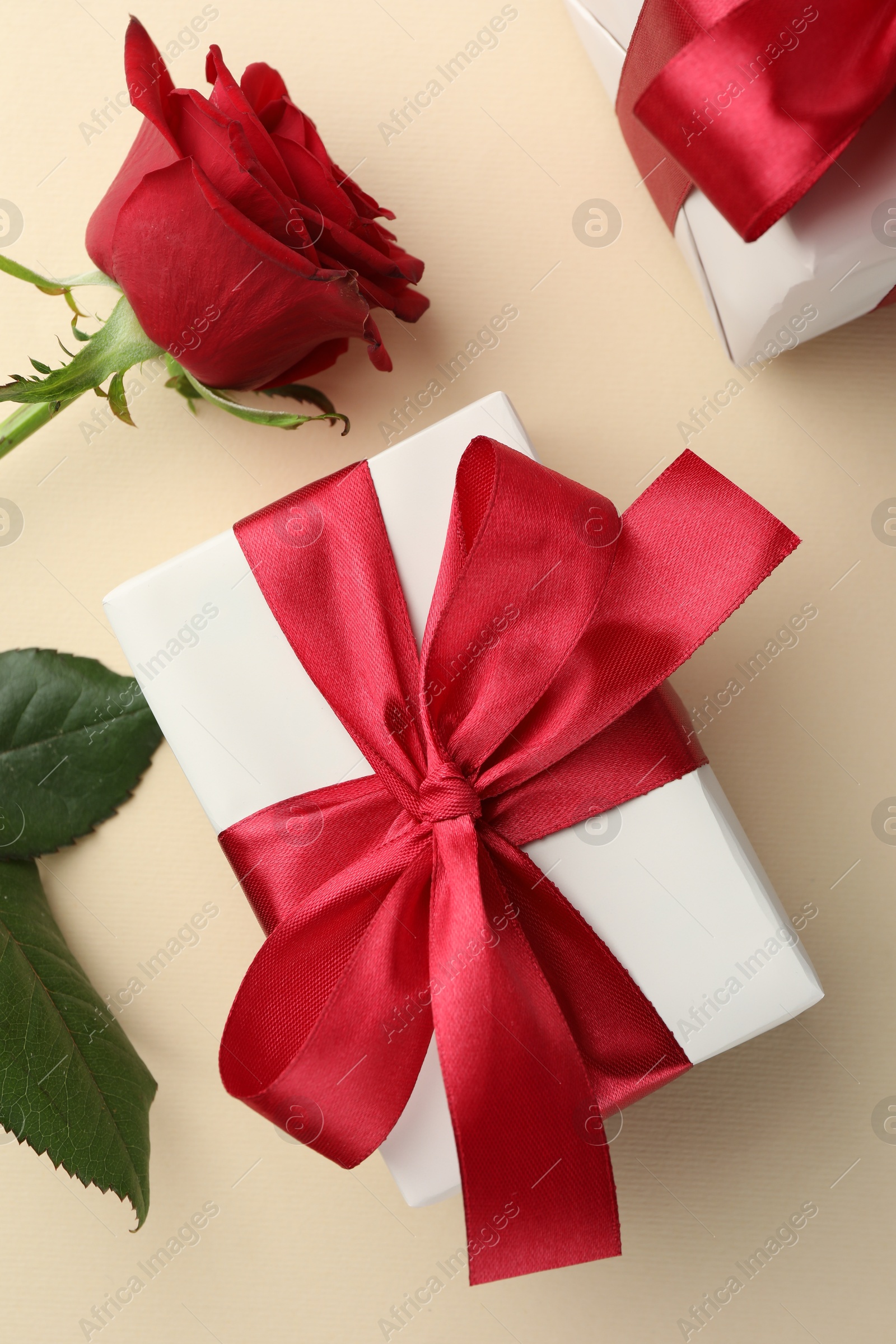 Photo of Beautiful gift box with red bow and rose on beige background, top view