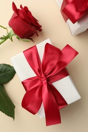 Beautiful gift box with red bow and rose on beige background, top view