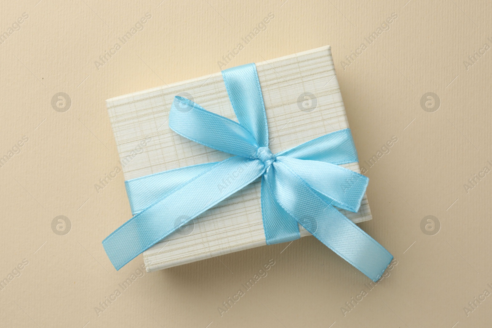 Photo of Beautiful gift box with light blue bow on beige background, top view