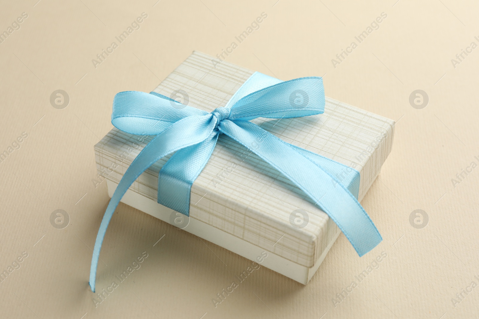 Photo of Beautiful gift box with light blue bow on beige background, closeup