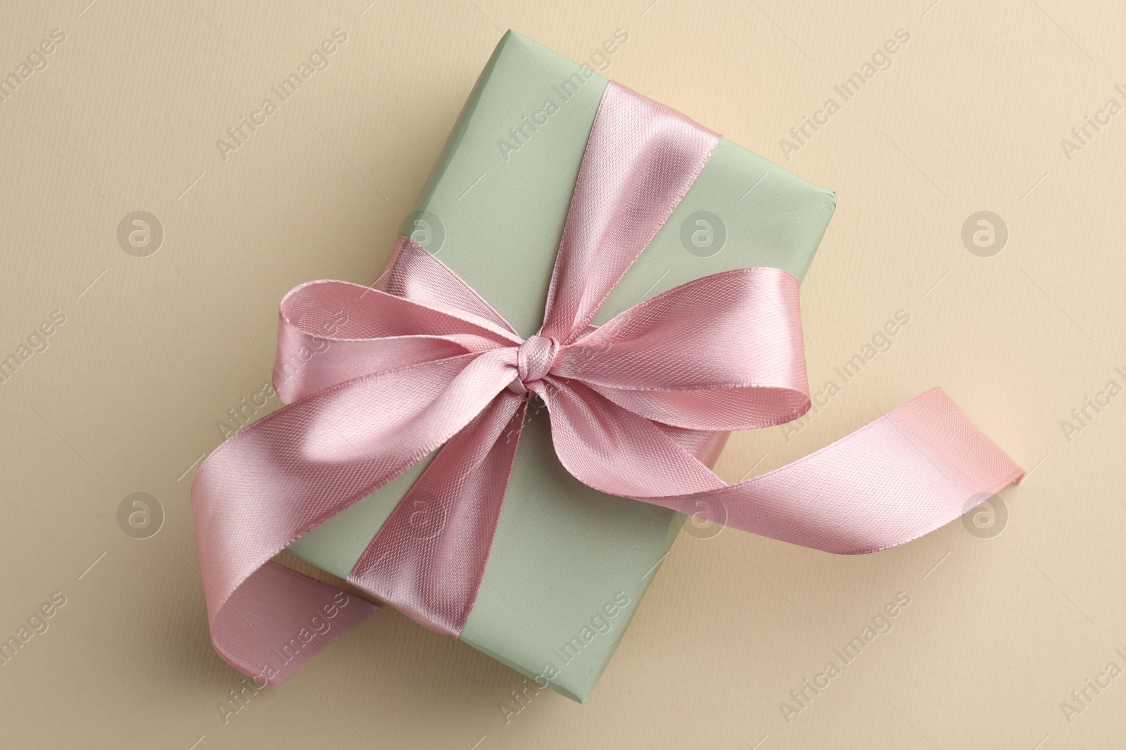 Photo of Beautiful gift box with pink bow on beige background, top view