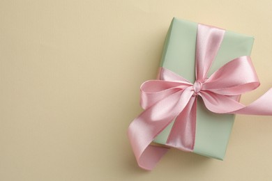 Photo of Beautiful gift box with pink bow on beige background, top view. Space for text