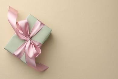 Photo of Beautiful gift box with pink bow on beige background, top view. Space for text