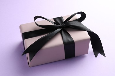 Beautiful gift box with black bow on violet background