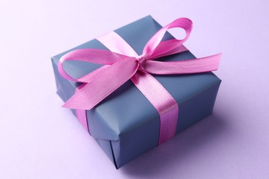 Photo of Beautiful gift box with pink bow on violet background, closeup