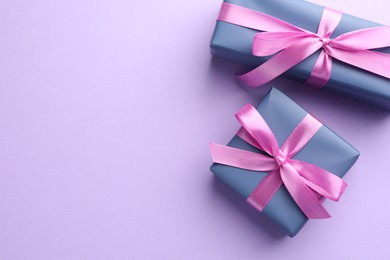 Beautiful gift boxes with pink bows on violet background, top view. Space for text