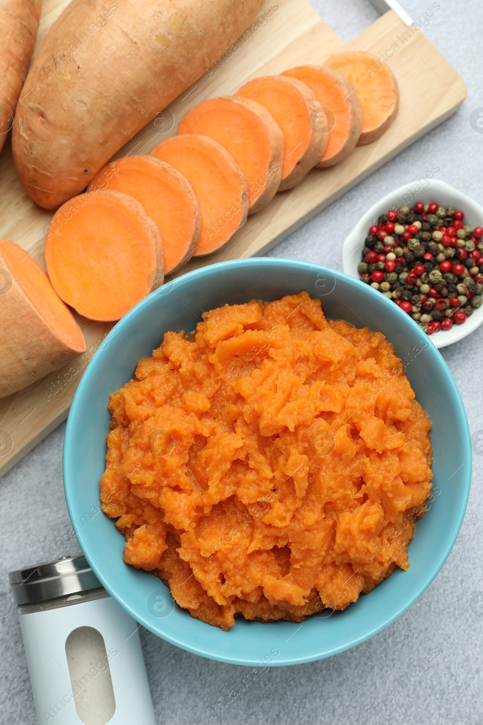 Photo of Tasty mashed sweet potato in bowl, fresh vegetables and spices on gray table, flat lay