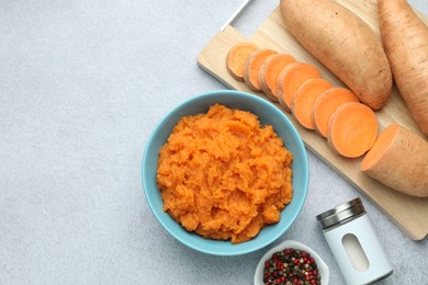 Photo of Tasty mashed sweet potato in bowl, fresh vegetables and spices on gray table, flat lay. Space for text