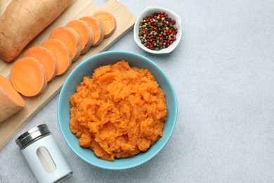 Photo of Tasty mashed sweet potato in bowl, fresh vegetables and spices on gray table, flat lay. Space for text