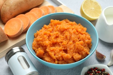 Photo of Tasty mashed sweet potato in bowl, fresh vegetables, spices, sauce and lemon on gray table, closeup