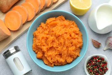 Photo of Tasty mashed sweet potato in bowl, fresh vegetables, spices, sauce and lemon on gray table, flat lay