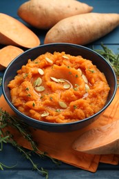 Photo of Tasty mashed sweet potato with pumpkin seeds in bowl, fresh vegetables and thyme on blue wooden table, closeup