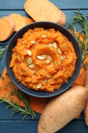 Photo of Tasty mashed sweet potato with pumpkin seeds in bowl, fresh vegetables, rosemary and thyme on blue wooden table, flat lay