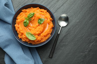 Photo of Tasty mashed sweet potato in bowl served on dark gray textured table, flat lay