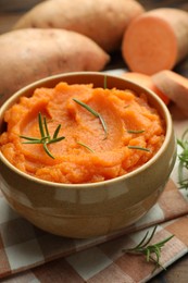 Photo of Tasty mashed sweet potato with rosemary in bowl and fresh vegetables on table, closeup