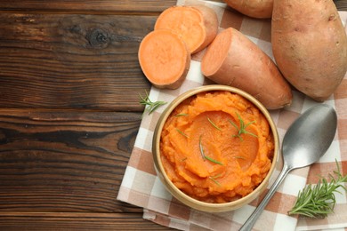 Photo of Tasty mashed sweet potato with rosemary in bowl, fresh vegetables and spoon on wooden table, flat lay. Space for text