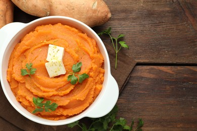 Photo of Tasty mashed sweet potato with butter in bowl, fresh vegetables and parsley on wooden table, flat lay. Space for text