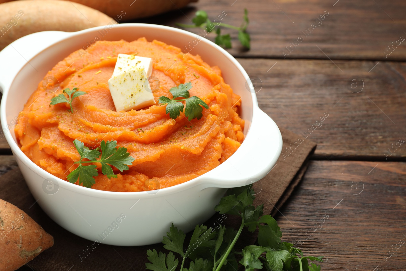 Photo of Tasty mashed sweet potato with butter and parsley in bowl on wooden table, closeup