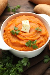 Photo of Tasty mashed sweet potato with butter in bowl, fresh vegetables and parsley on table, closeup