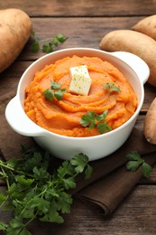 Photo of Tasty mashed sweet potato with butter in bowl, fresh vegetables and parsley on wooden table, closeup