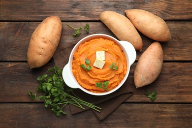 Photo of Tasty mashed sweet potato with butter in bowl, fresh vegetables and parsley on wooden table, flat lay