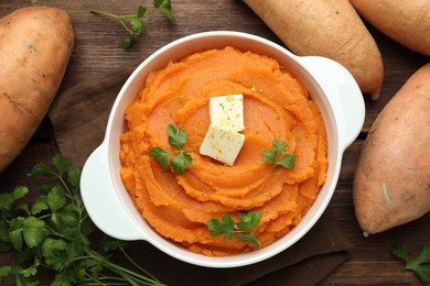 Photo of Tasty mashed sweet potato with butter in bowl, fresh vegetables and parsley on wooden table, flat lay