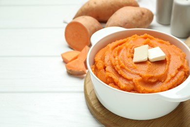 Photo of Tasty mashed sweet potato with butter in bowl and fresh vegetables on white wooden table, closeup