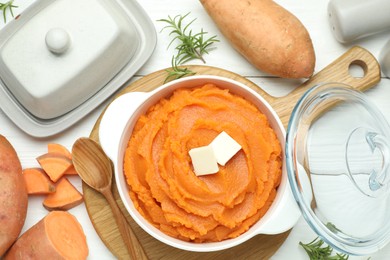 Photo of Tasty mashed sweet potato with butter in bowl, spoon, fresh vegetables and spices on white wooden table, flat lay