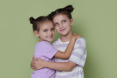 Portrait of cute little sisters on light green background