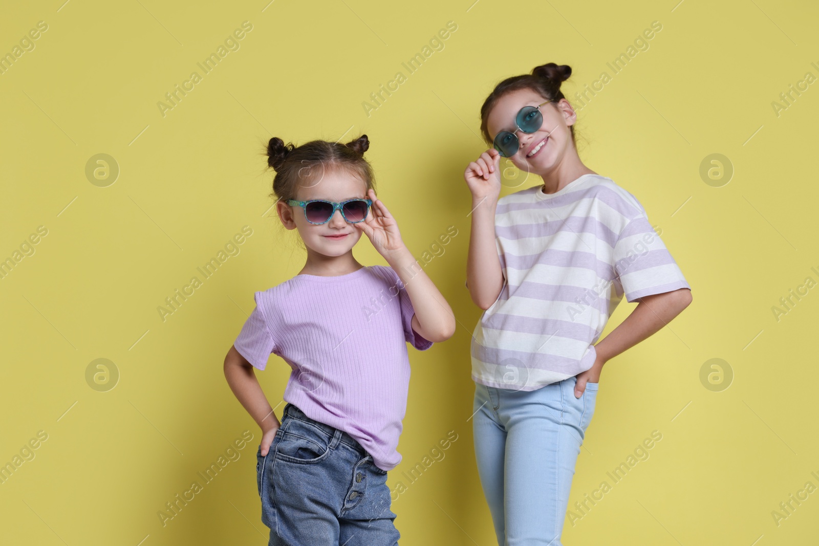 Photo of Portrait of cute little sisters on yellow background