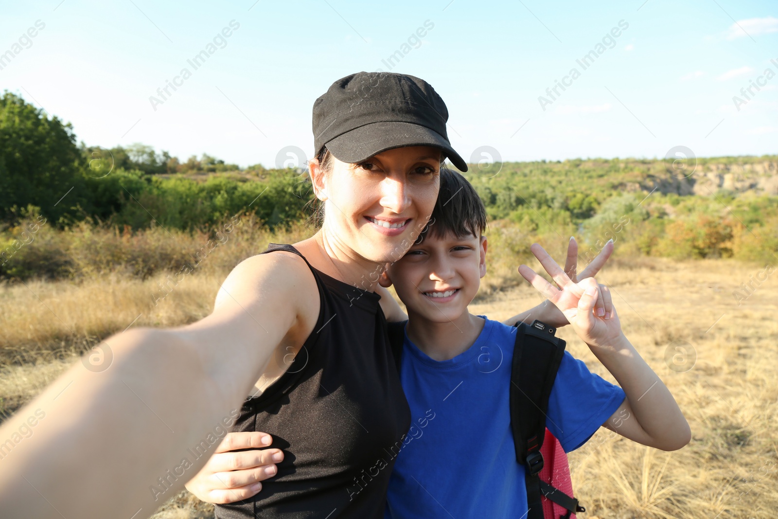 Photo of Smiling mother taking selfie with her son and showing peace signs outdoors