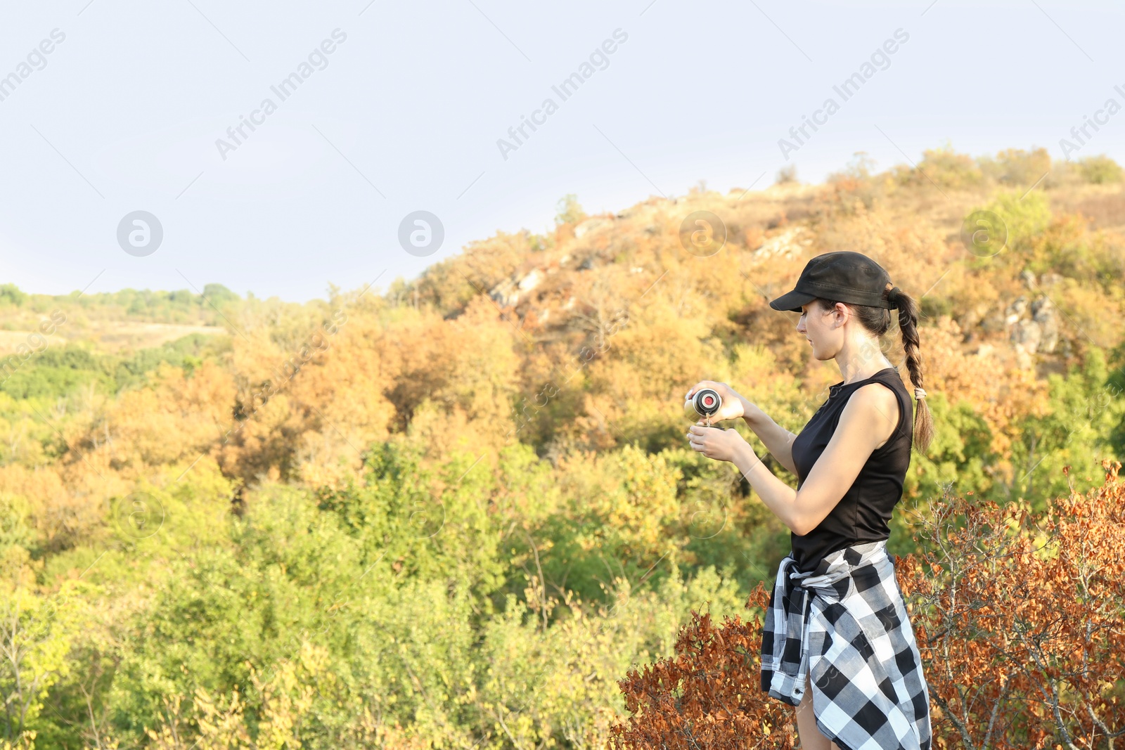 Photo of Woman pouring tea from thermos into cup near tree outdoors. Space for text