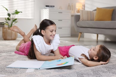 Cute little sisters with book at home