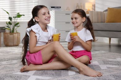 Cute little sisters with glasses of juice at home