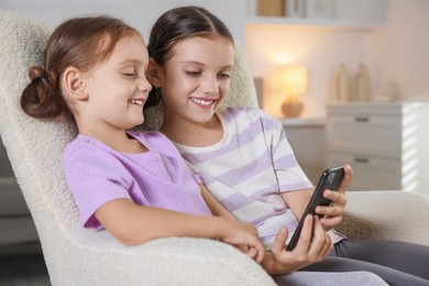 Photo of Cute little sisters using smartphone at home