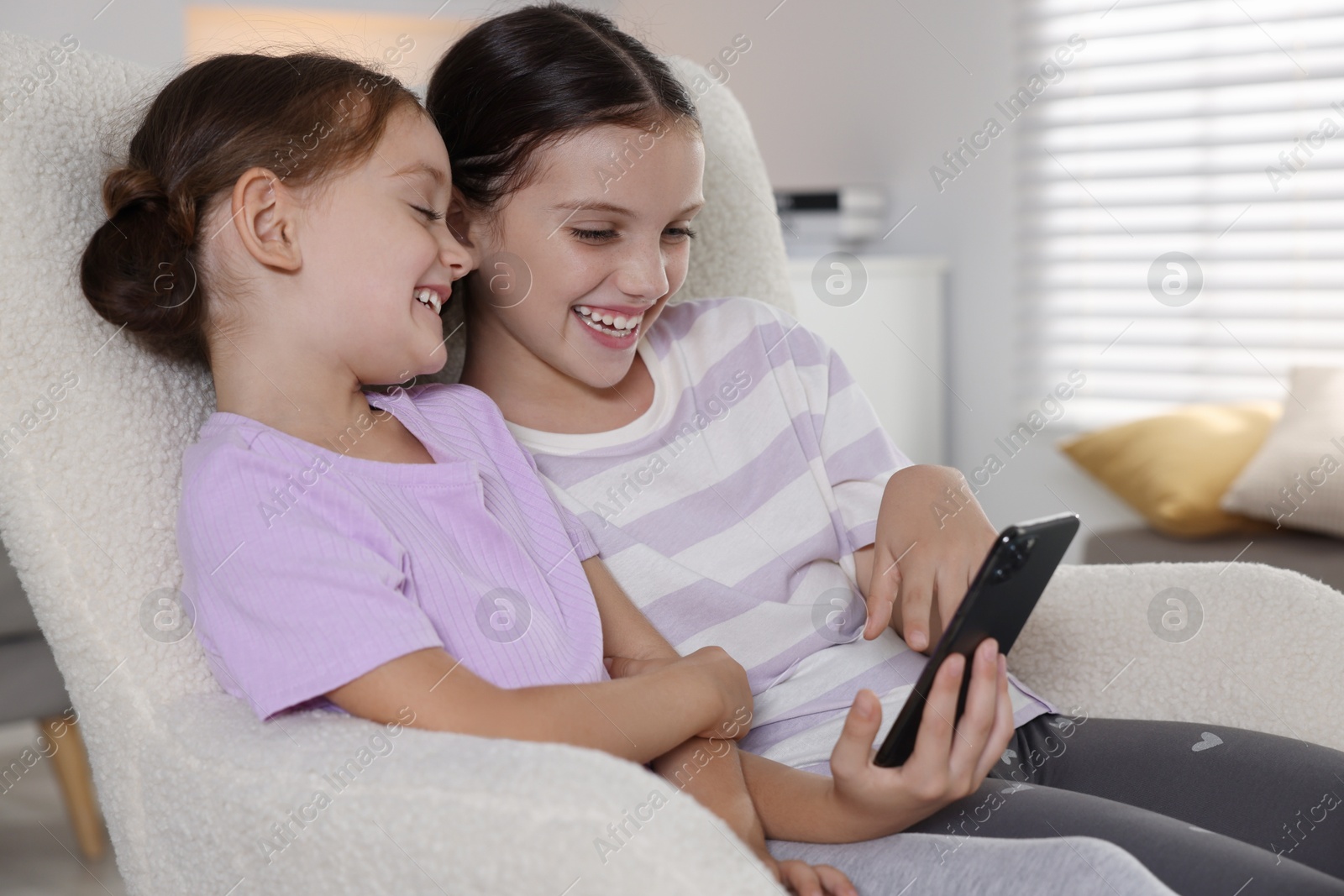 Photo of Cute little sisters using smartphone at home