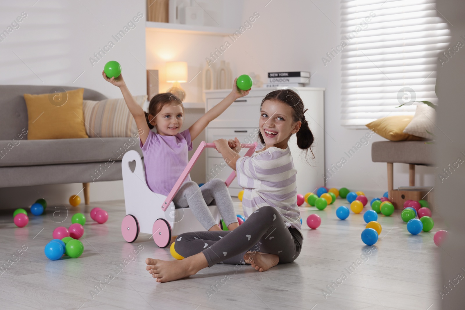 Photo of Cute little sisters playing with wooden stroller at home