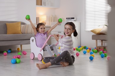 Photo of Cute little sisters playing with wooden stroller at home